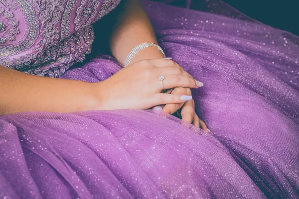 Close-up of hands resting gracefully on a purple sparkling dress, showcasing elegance.