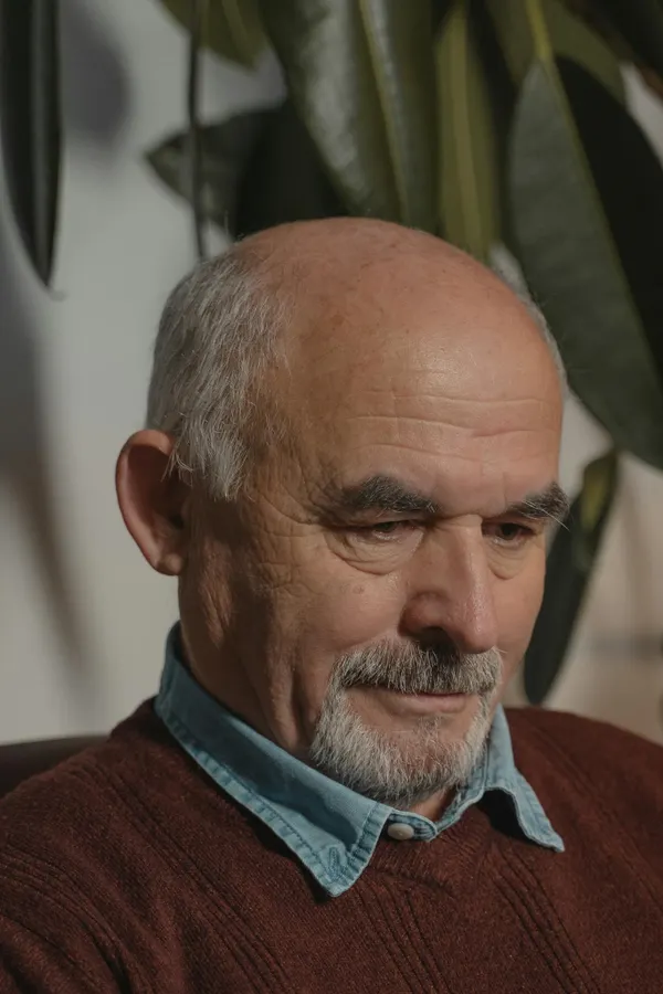 Close-up portrait of a thoughtful senior man with white hair and a goatee indoors.
