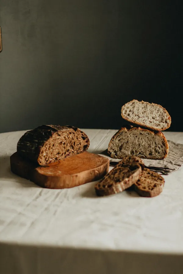 Delicious homemade cut loaves of black and white bread placed on white table with wooden cutting board on gray background in