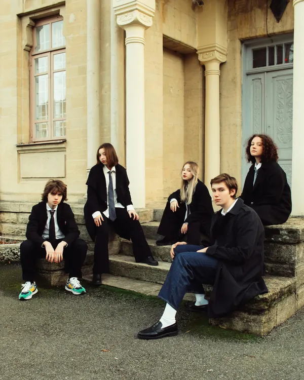 Five teenagers in school uniforms seated on steps of a classical building, Russia.