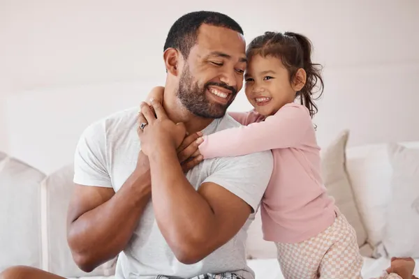 Smiling daughter hugs her dad on the bed; warm father–daughter bond, pure “Girl Dad” energy.