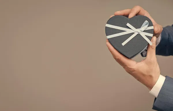 Hands holding corporate giftbox on grey background with copy space love date shopping sale