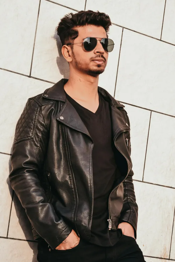 Man in Black Leather Jacket Leaning on White Concrete Wall