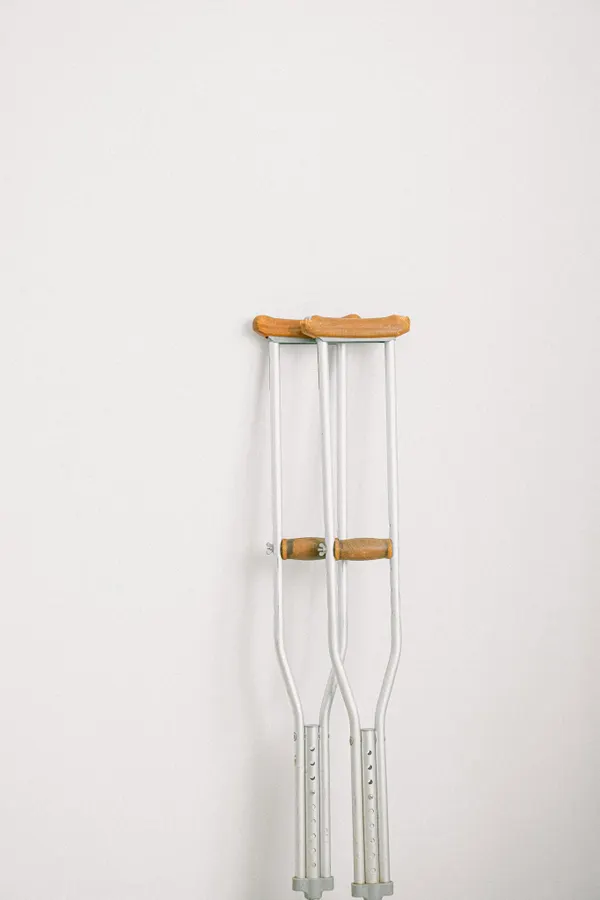 Minimalist image of crutches leaning on a white wall indoors.