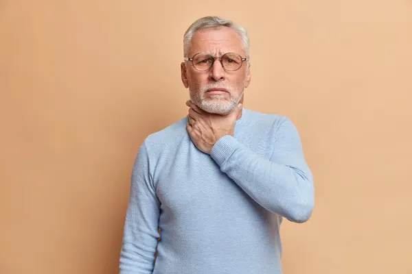 Free photo old handsome bearded man touches neck suffocates because of painful strangle feels pain in throat while swallow we