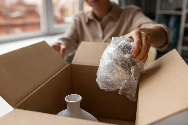 Packing fragile objects at home—protective wrap cushioning a delicate vase inside a box.