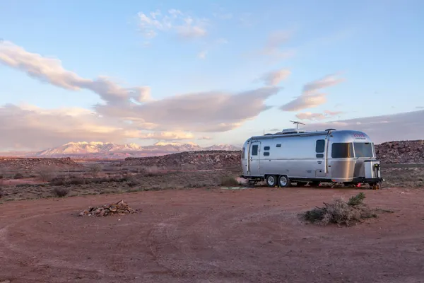 Silver trailer in desert landscape at sunset with mountains in the background.
