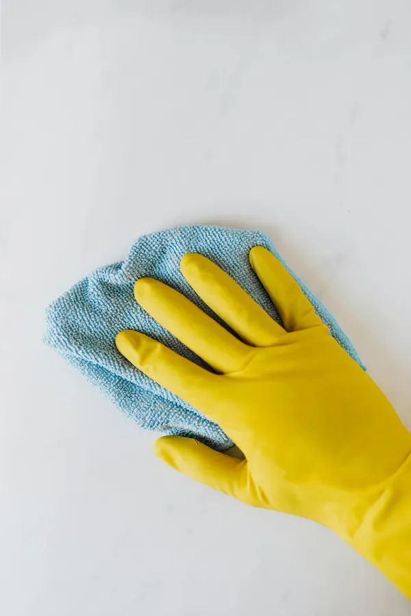 Yellow gloved hand wiping surface with blue cloth, concept of cleaning and hygiene.