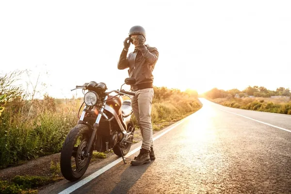 Young handsome man posing near his motorbike at countryside road.