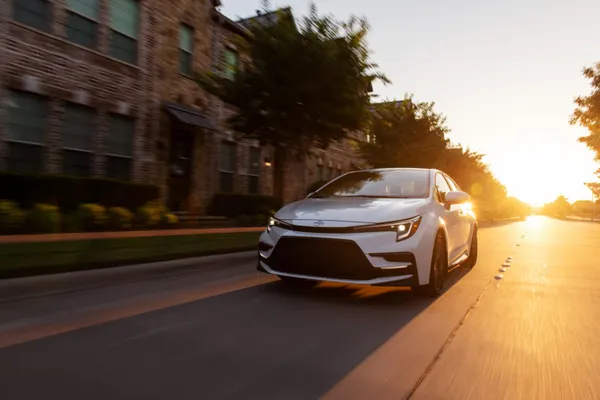 2026 Toyota Corolla Cross XLE AWD driving on city road during sunset exterior view