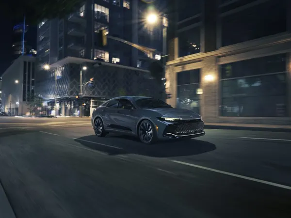 2026 Toyota Crown Nightshade driving through a downtown city street at night with LED headlights and matte-black wheels
