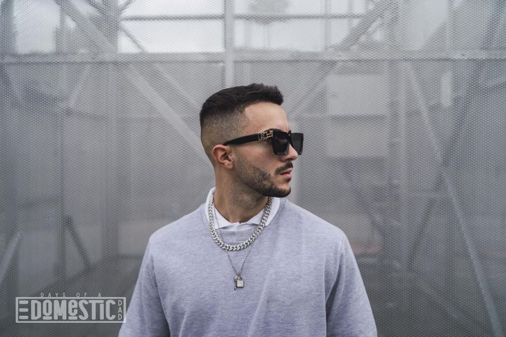 Stylish young attractive man wearing a sweater over a shirt with necklaces and sunglasses