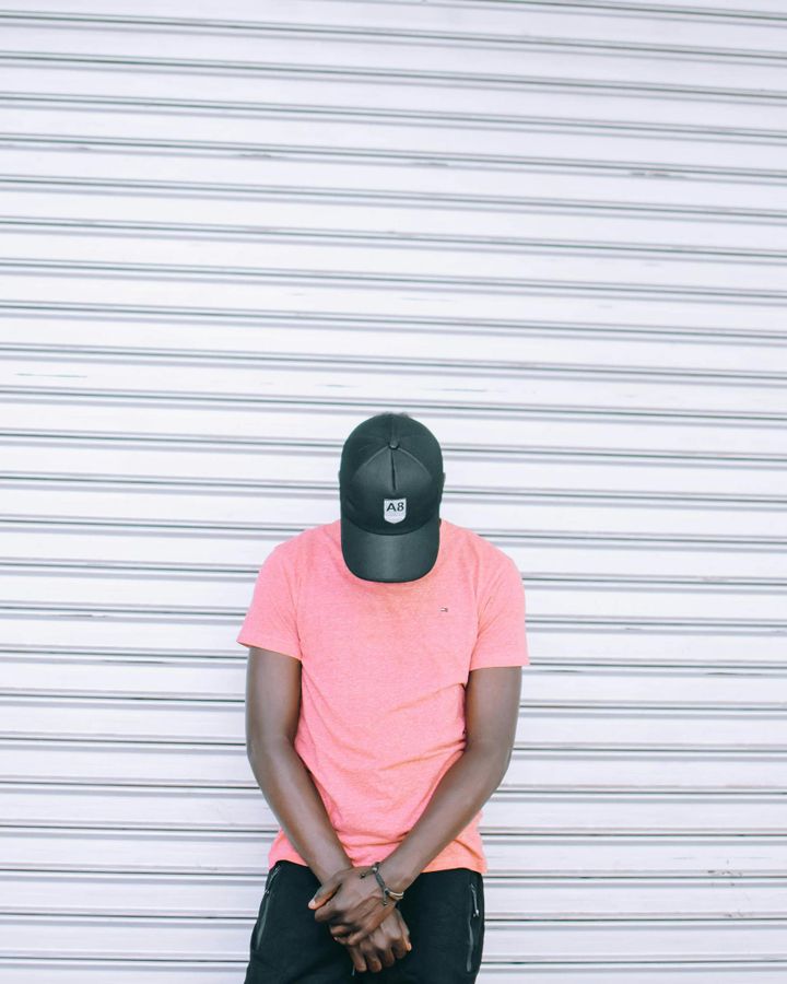 A casual portrait of a man wearing a pink shirt and cap against a striped background.