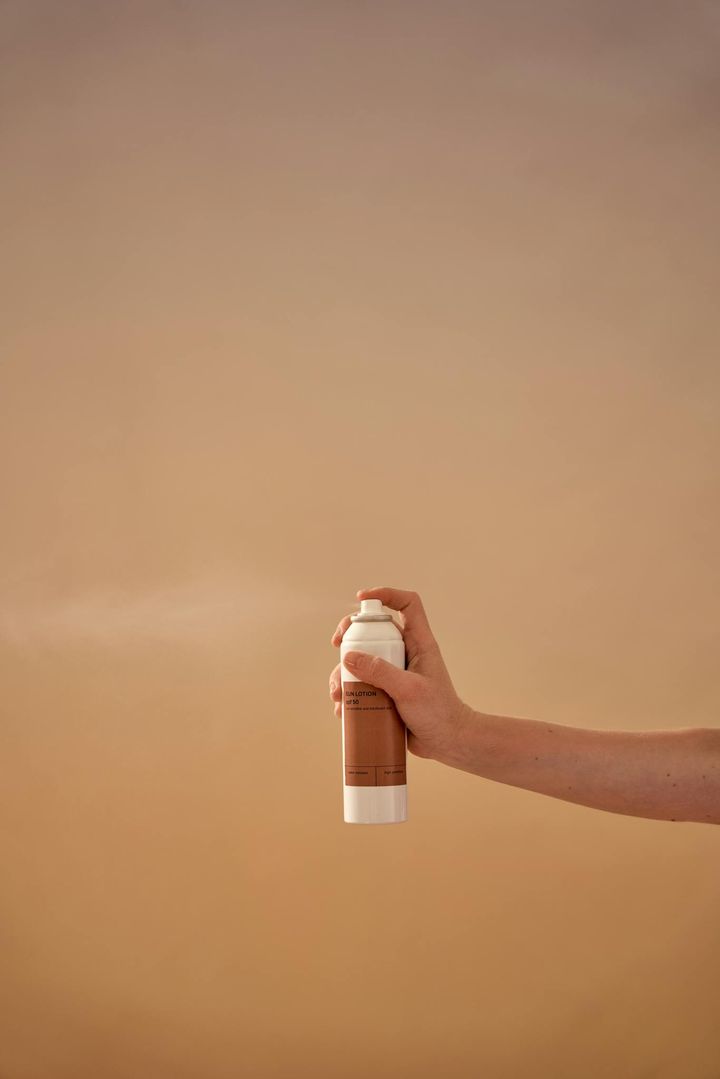 A clean studio shot of a hand holding a sunscreen spray bottle with a neutral background.