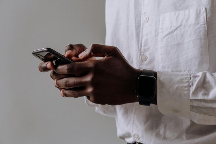 A close-up shot of a person wearing a smartwatch and typing on a smartphone indoors.