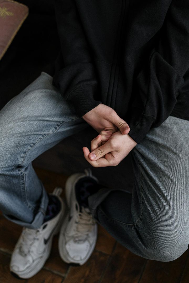 A young man in casual attire sitting with hands clasped, expressing contemplation.