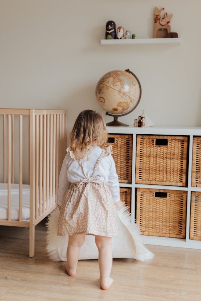 Back view of unrecognizable cute little girl in casual dress holding white carpet in hands while playing in light room at hom