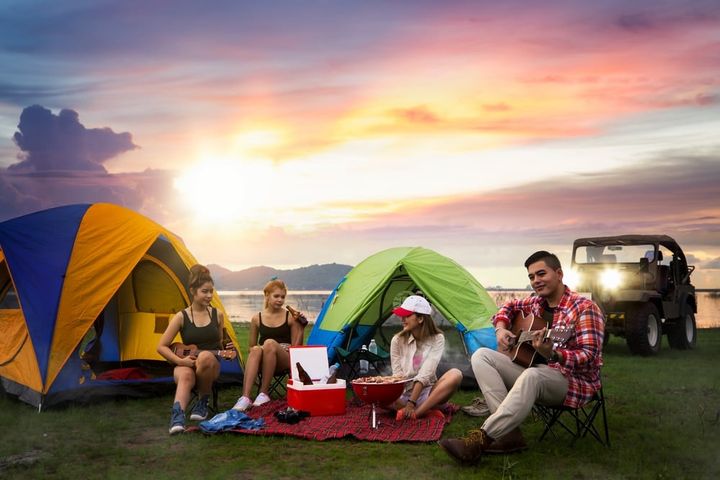 Camping of asian man and women group, relaxing, sing a song and cooking, with ligh from car and tent