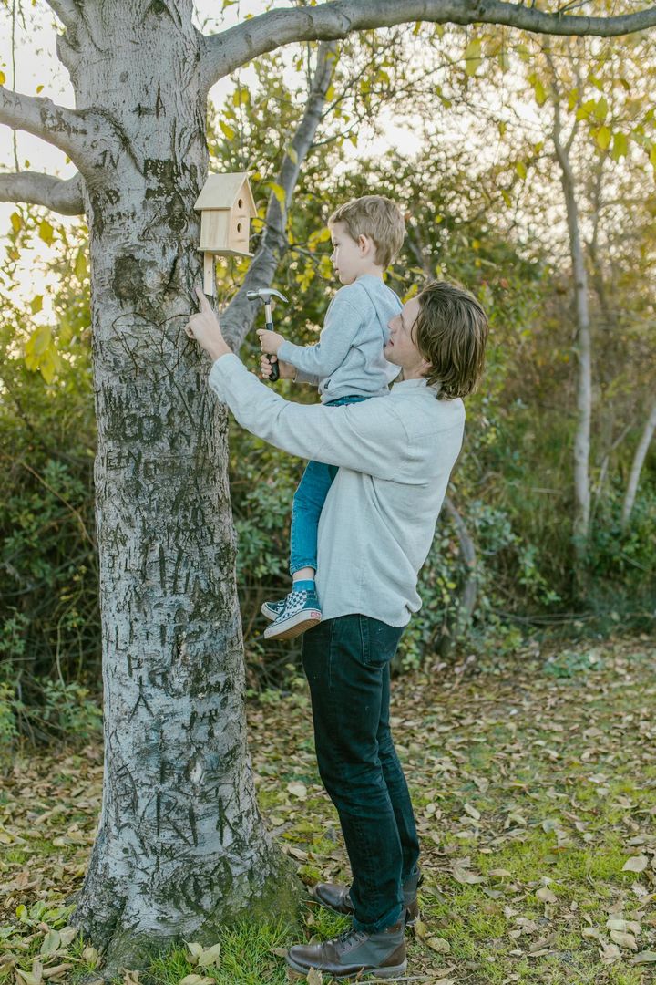 Father and son bonding while installing a birdhouse on a tree outdoors.