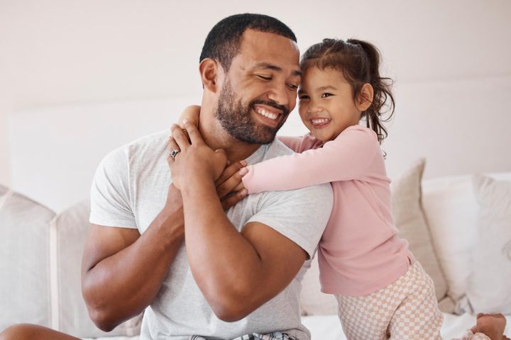 Smiling daughter hugs her dad on the bed; warm father–daughter bond, pure “Girl Dad” energy.