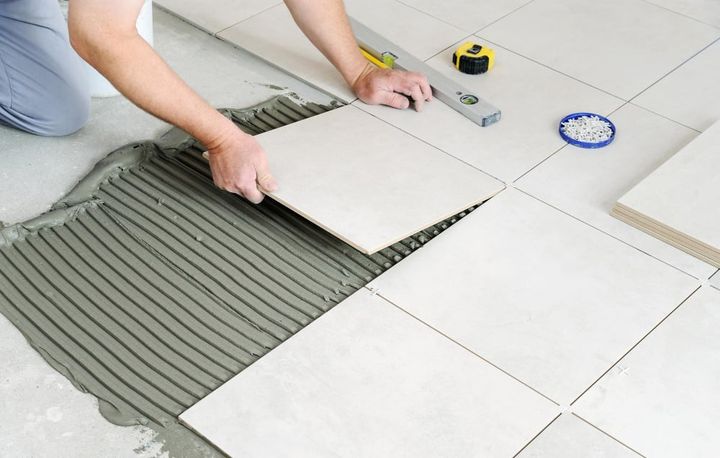 Photo the hands of the worker are laying the ceramic tile on the floor.