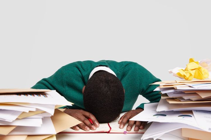 Free photo stressful workaholic keeps head down on desk, feels tired and overworked, has much work, prepares for upcoming exa