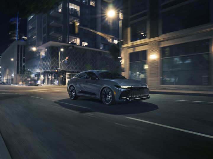 2026 Toyota Crown Nightshade driving through a downtown city street at night with LED headlights and matte-black wheels