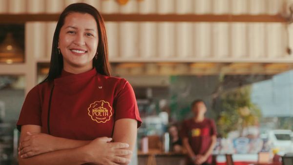 Yasmine, proprietária do Barracão do Poeta, sorri em frente à cafeteria usando uniforme
