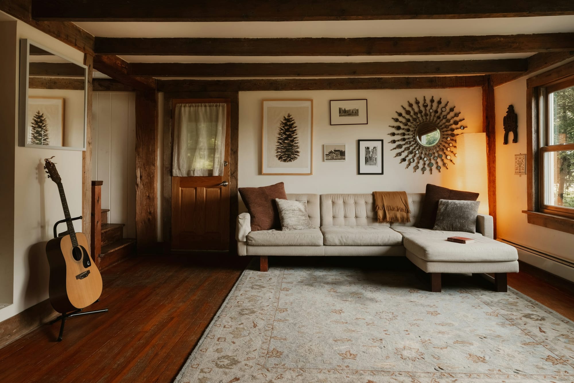 A lived-in living room with a cream sectional, warm wood beams and lamplight.