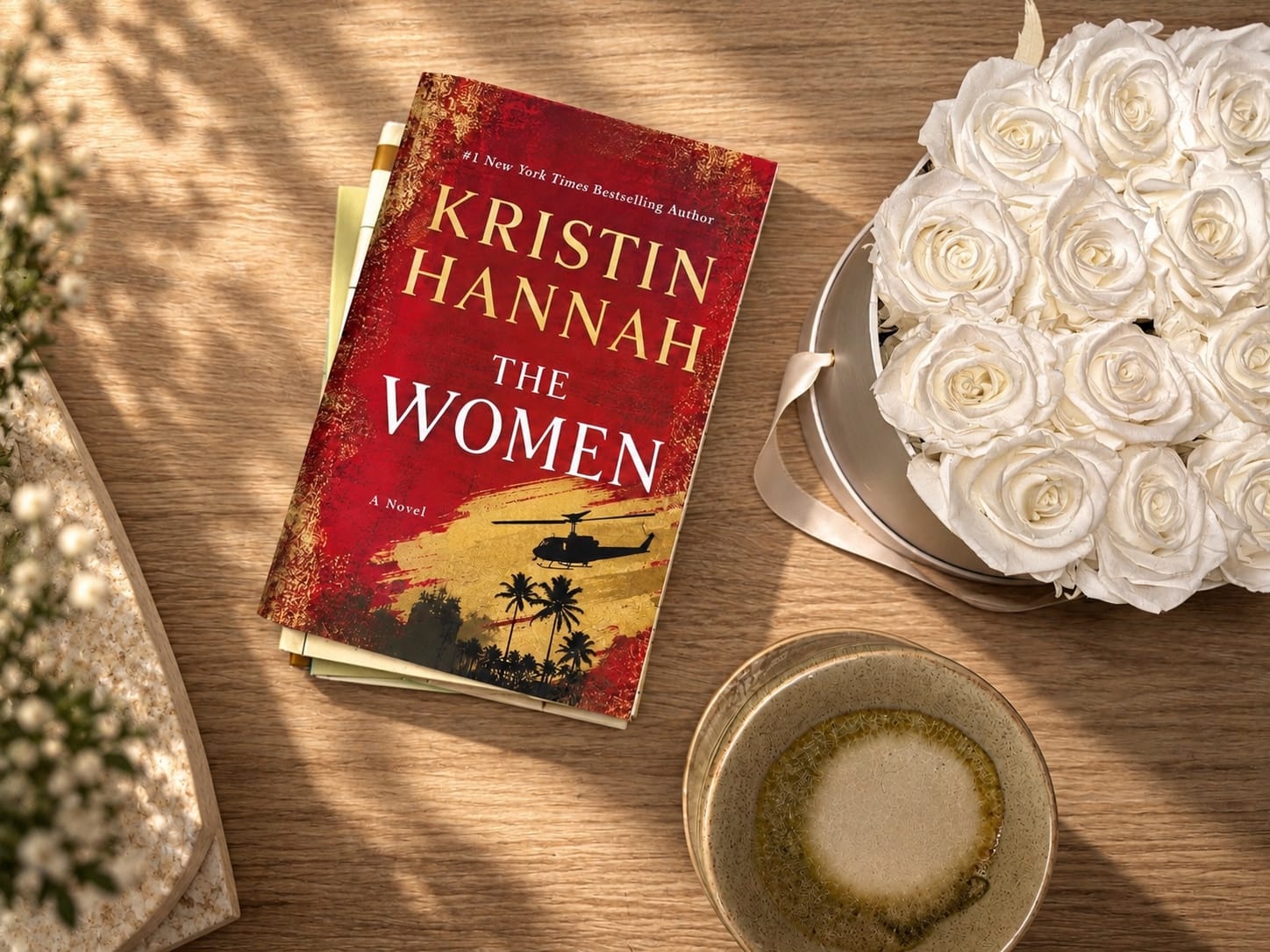 A physical copy of The Women by Kristin Hannah photographed on a wooden table in warm natural light.