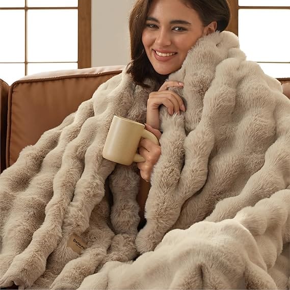 Neutral faux fur throw blanket draped around a seated woman