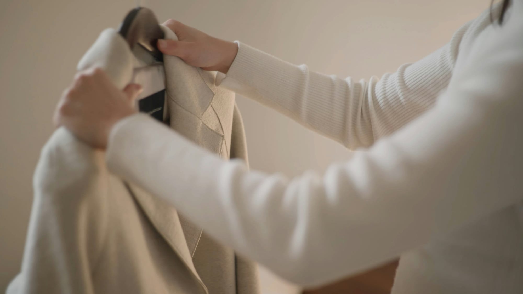 Hands fitting an ivory tailored jacket on a hanger.