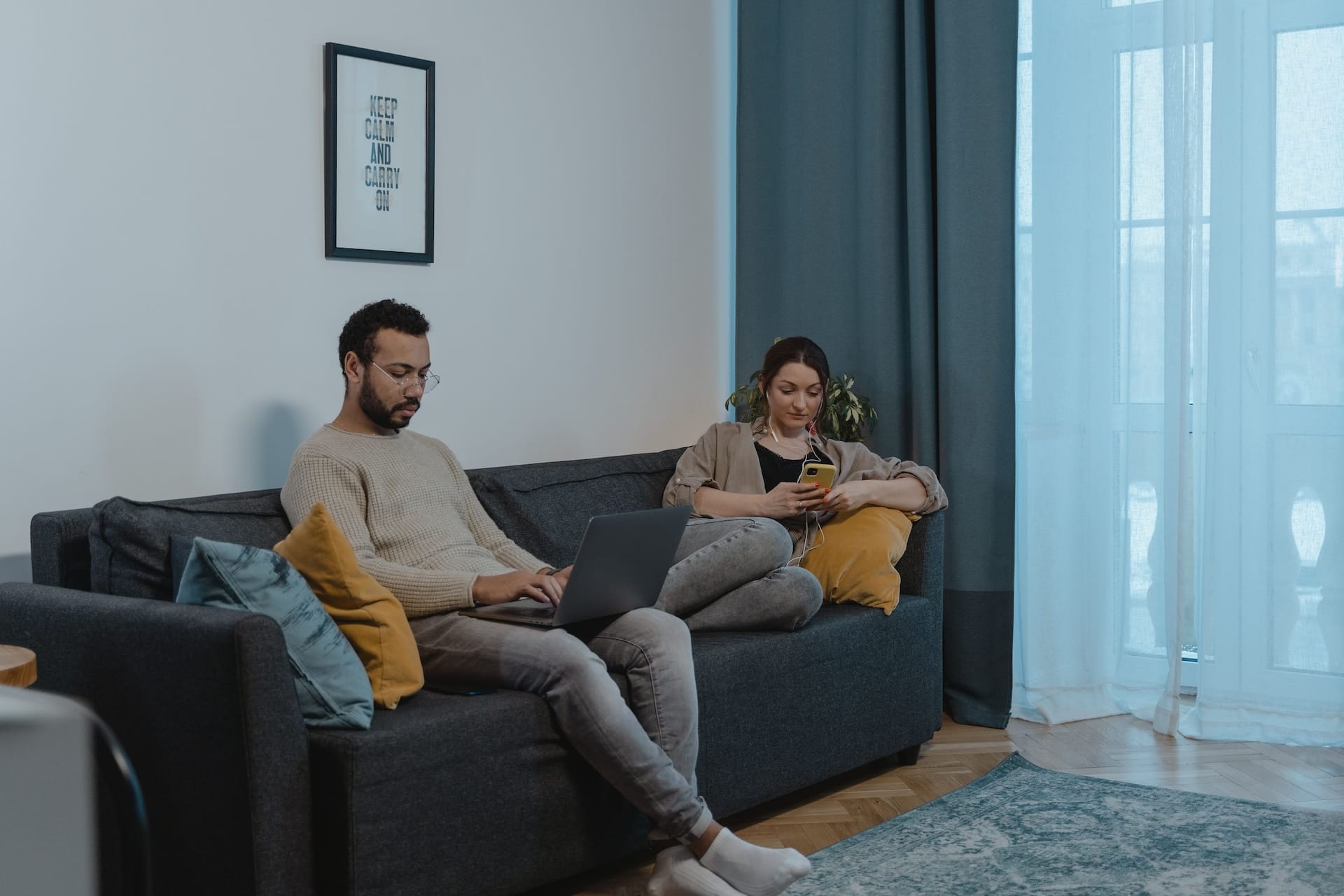A photo of two people at opposite ends of a sofa, uninterested in each other