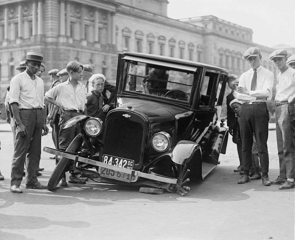 A photo showing a broken down car and a lot of people discussing it