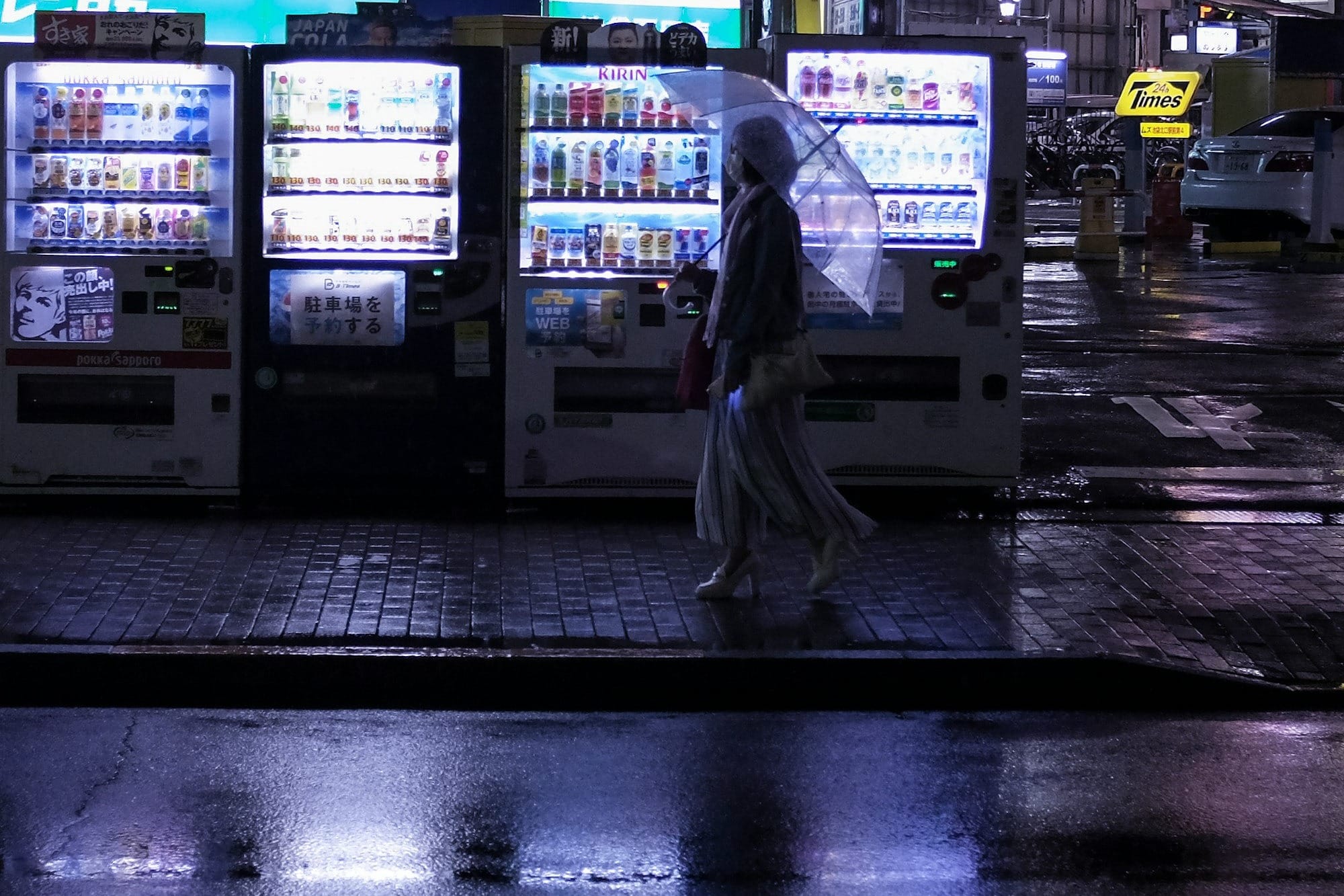Woman with a clear umbrella walking by a row of vending machines in Japan