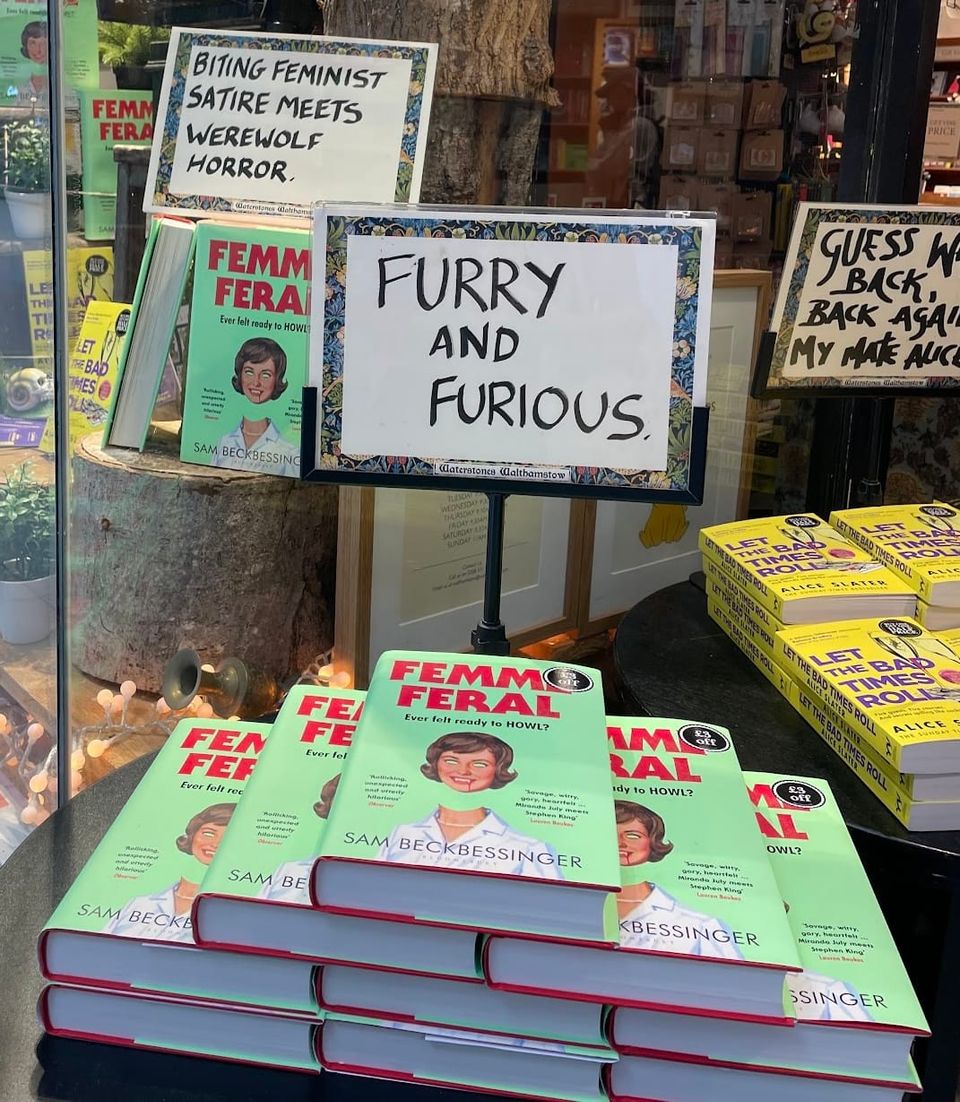 A pile of Femme Feral books in front of a sign that says "Furry and Furious"