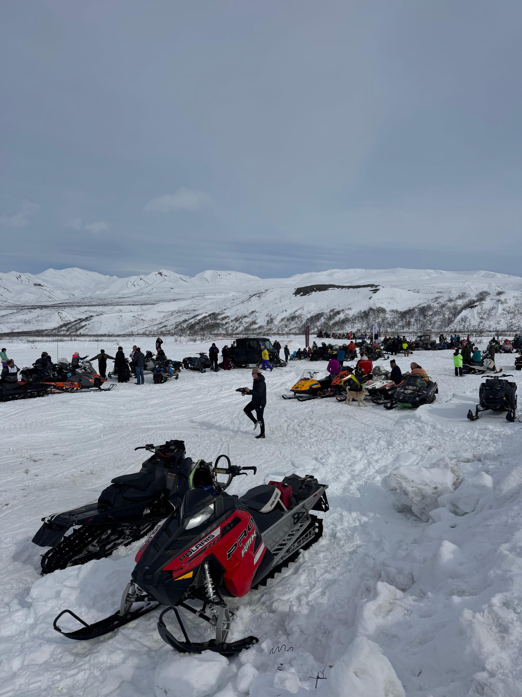 Arctic Man Alaska crowd gathered with snowmachines lined up in snowy valley during race event