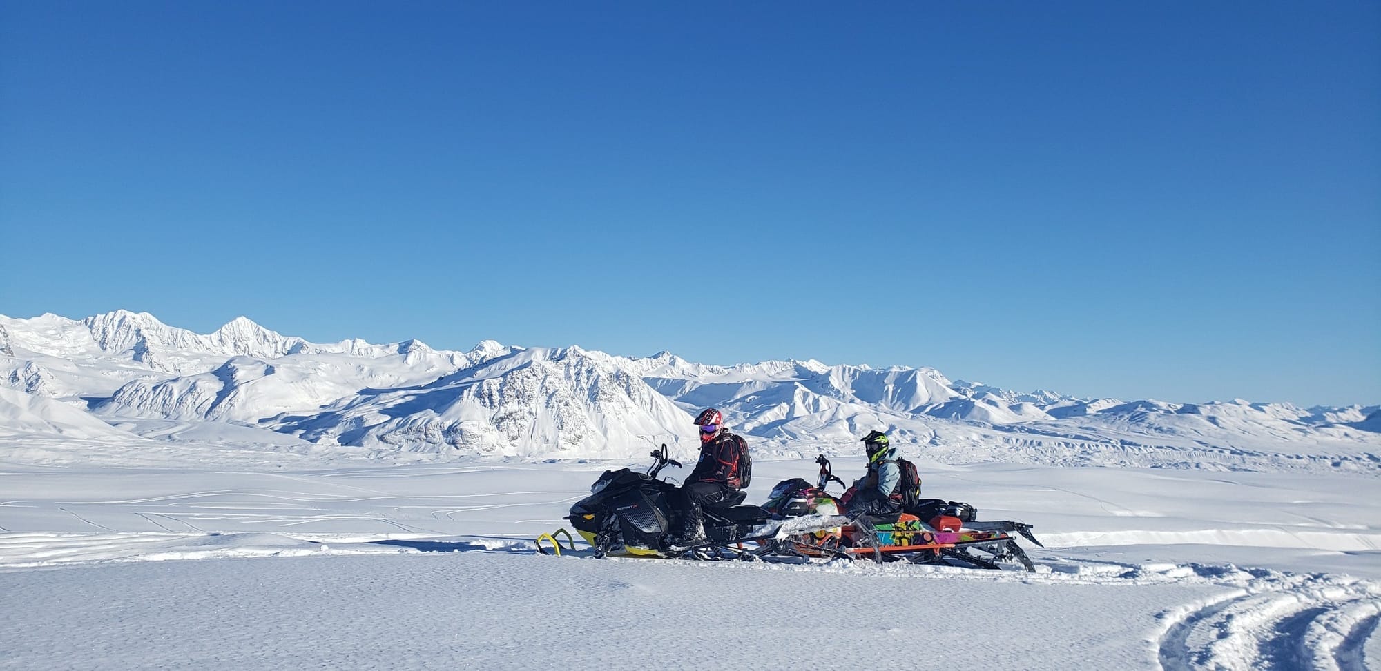 snowmachines crossing open backcountry at Arctic Man Alaska with Alaska Range mountains in the background