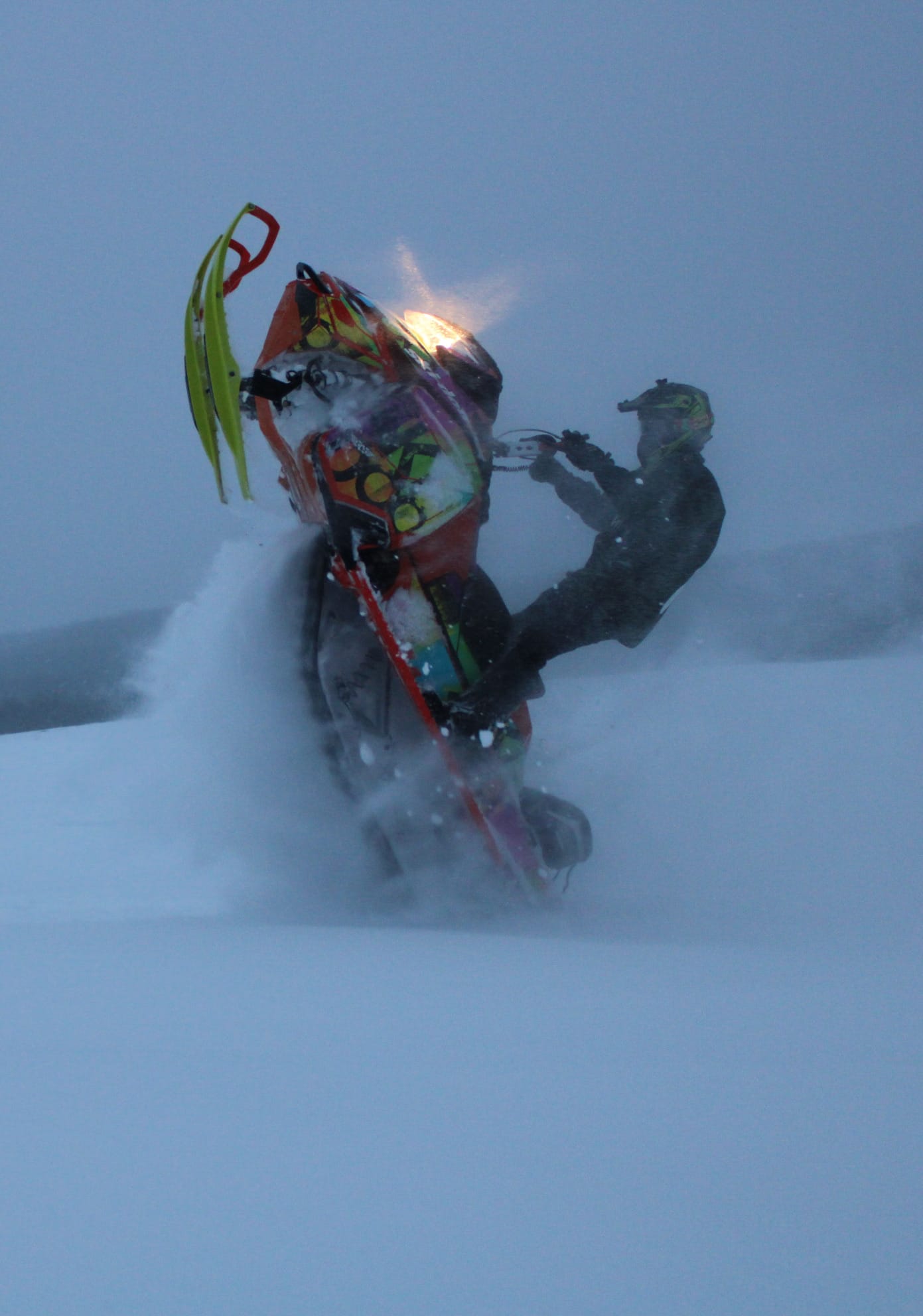 An Alaska snowmachine rider pulling a wheelie in deep powder during high intensity backcountry riding