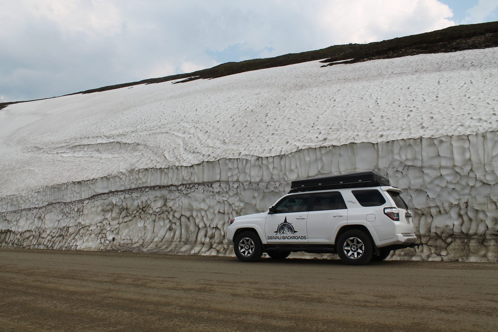 White SUV with a rooftop tent set up, parked by a big snow wall