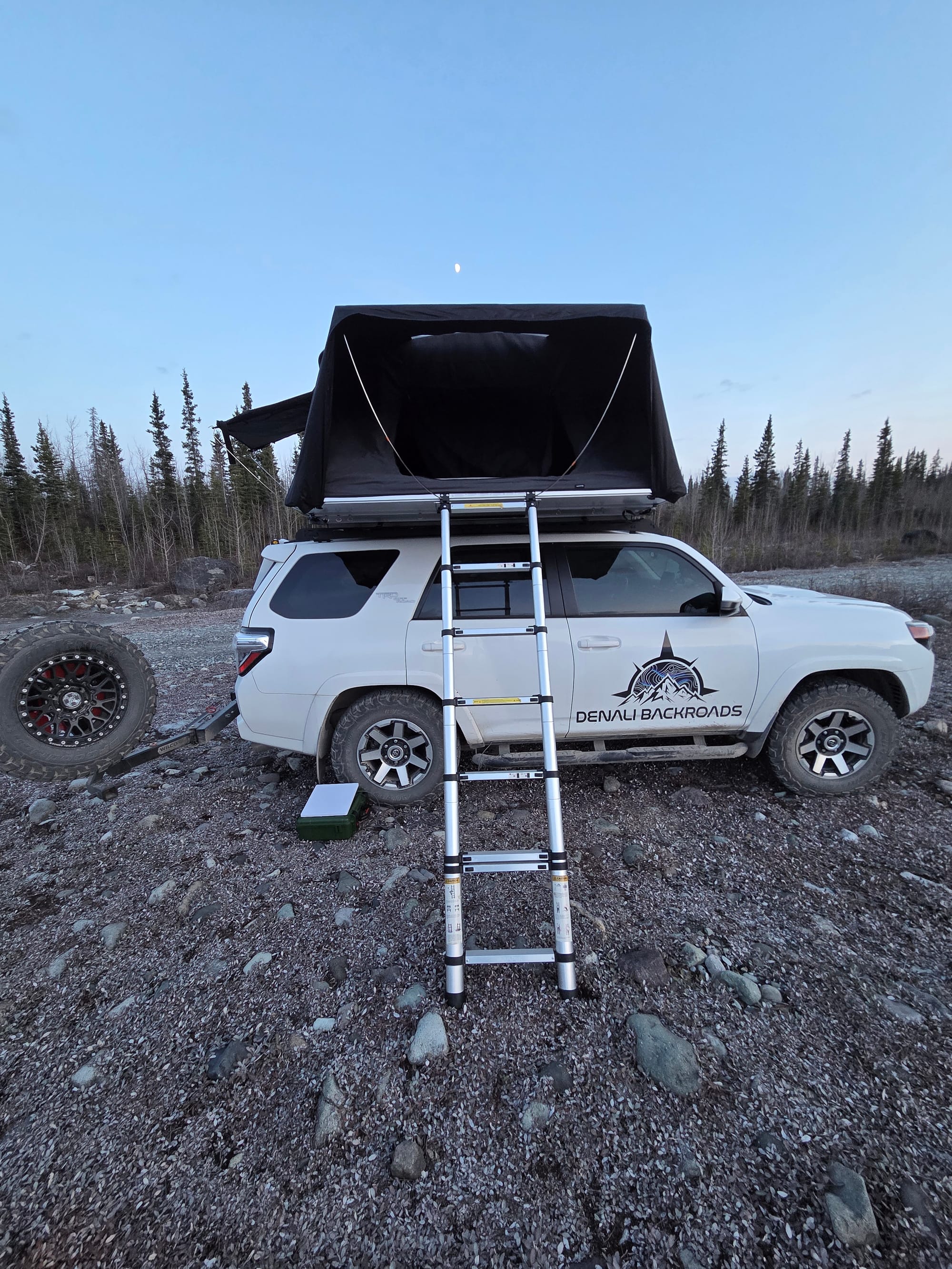 White Toyota 4Runner with rooftop tent deployed and ready for camping in the Alaska wilderness.