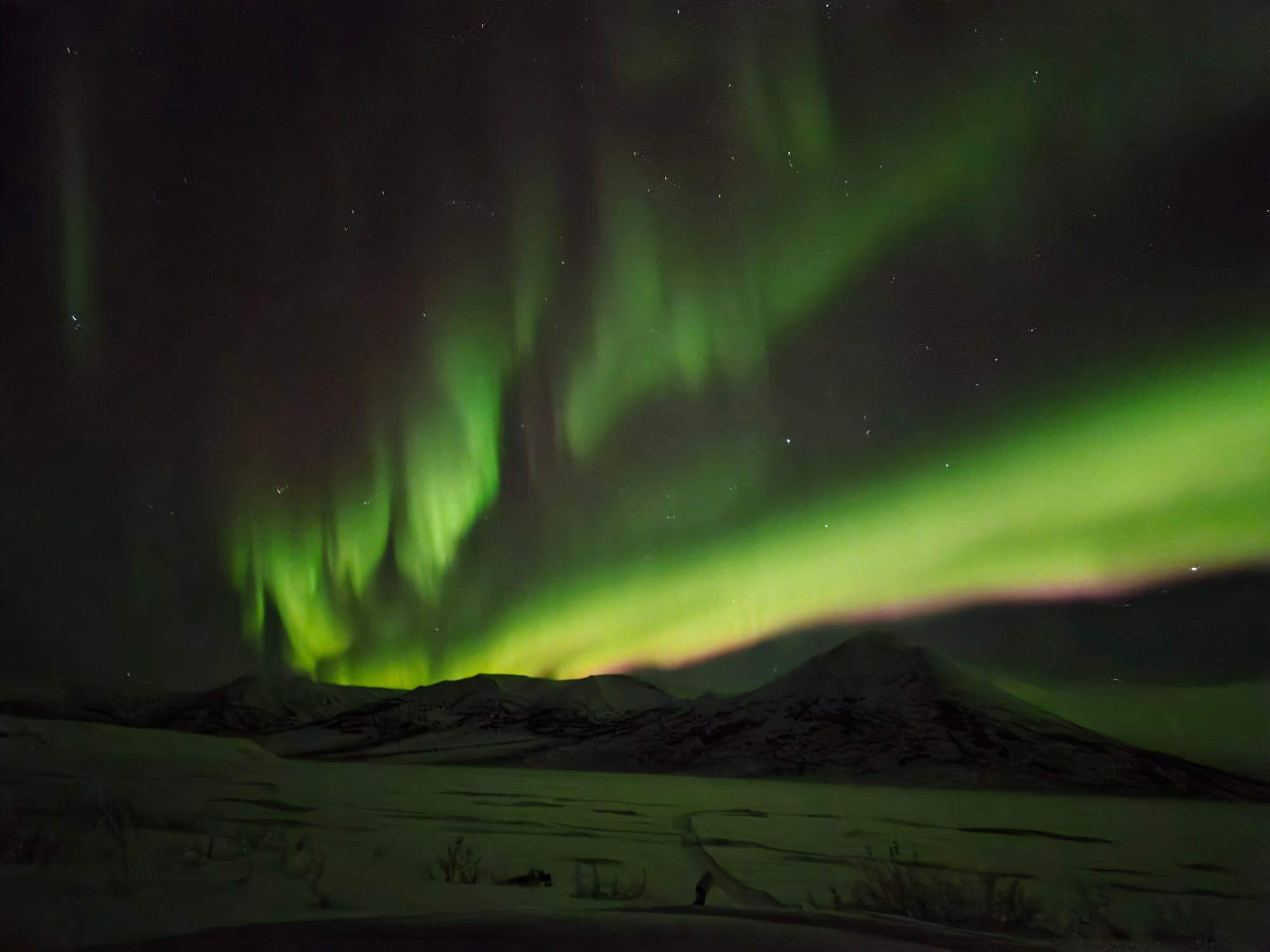 Bright green Northern Lights dancing above snow-covered mountains in Alaska