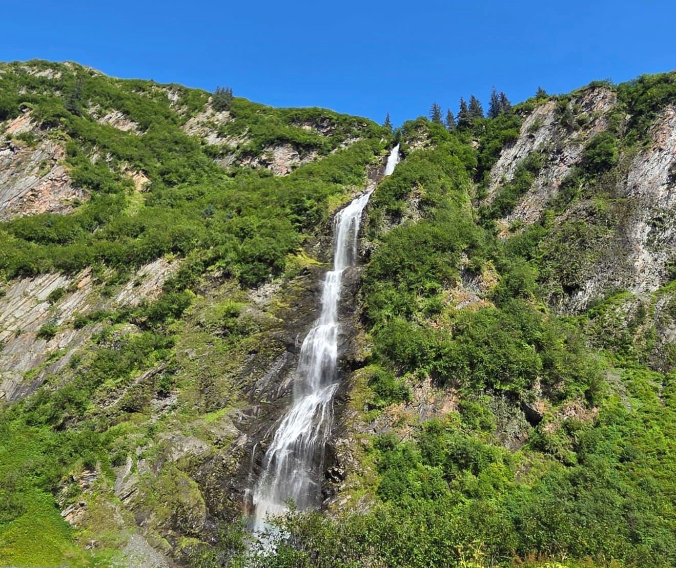 Tall waterfall cascading down rocky hillside in Alaska during summer
