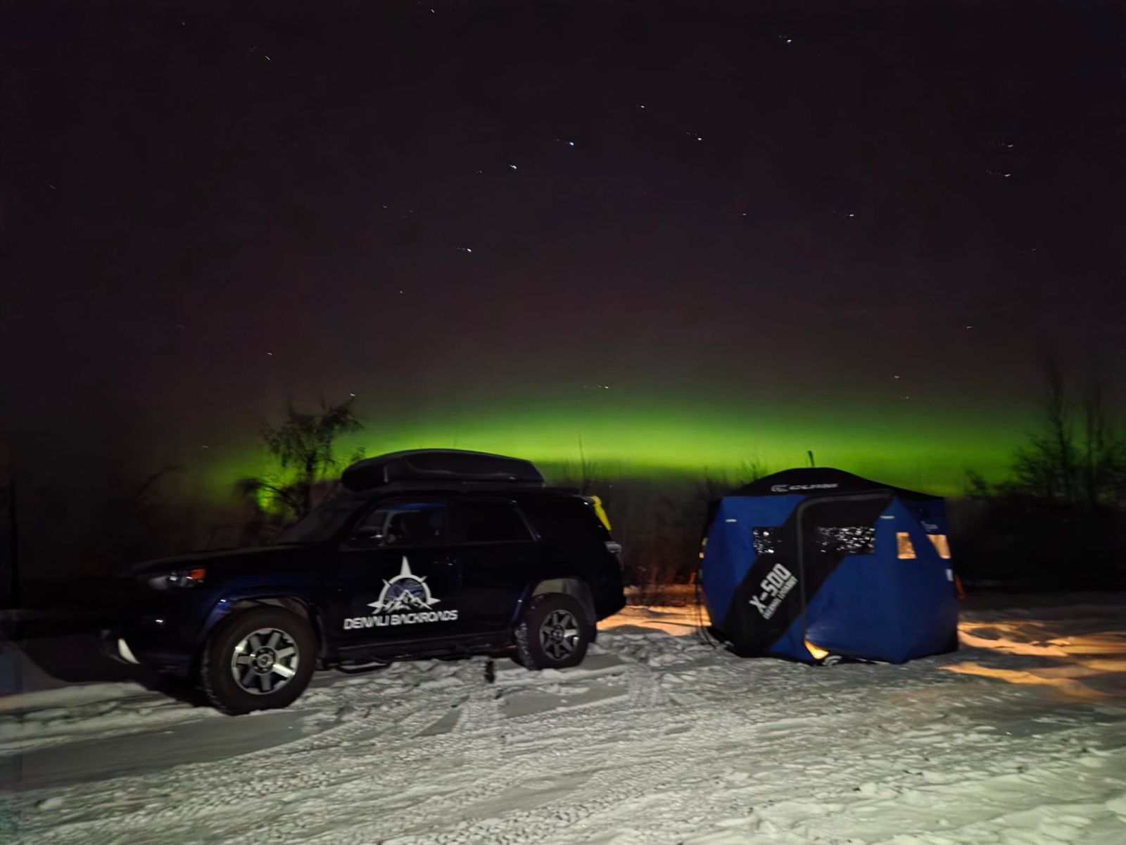 A cold night in Fairbanks Alaska with snow covered landscape with green northern lights spread across the night sky.
