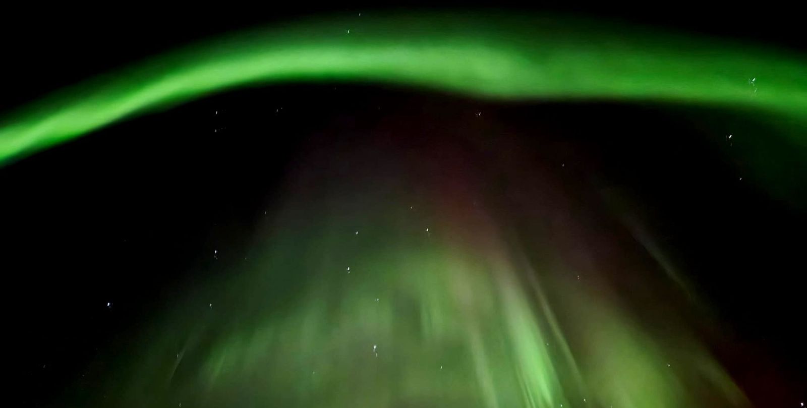 Northern lights glowing over a dark Alaskan ski with many stars.  