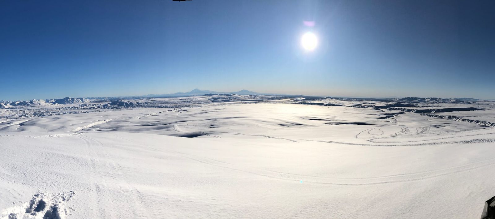 Arctic Man Alaska backcountry with snowmachine tracks across a vast snowy valley under bright winter sun