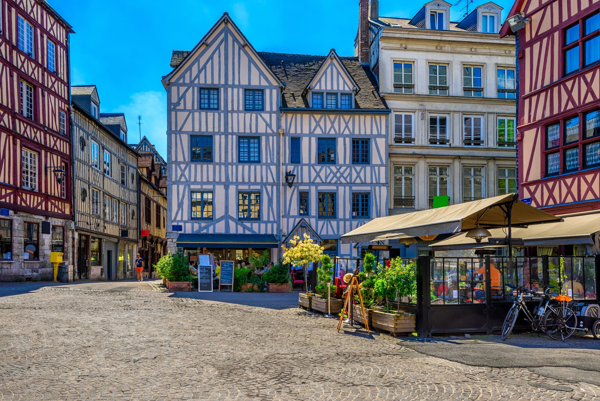 A town square in Rouen, France, with half-timbered houses and seating outside a restaurant