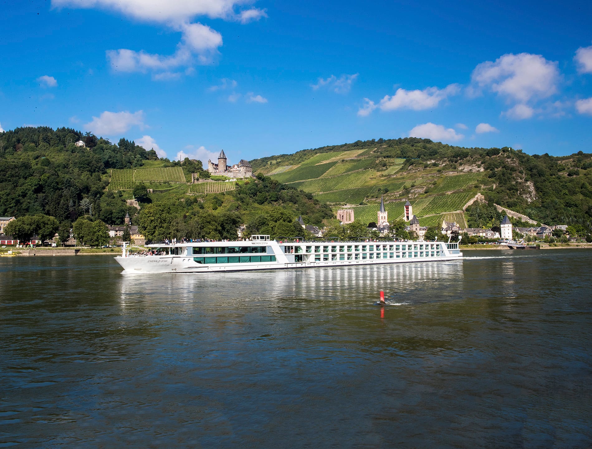 An image of a river cruise ship sailing past a small town with a castle on the hill during a sunny day