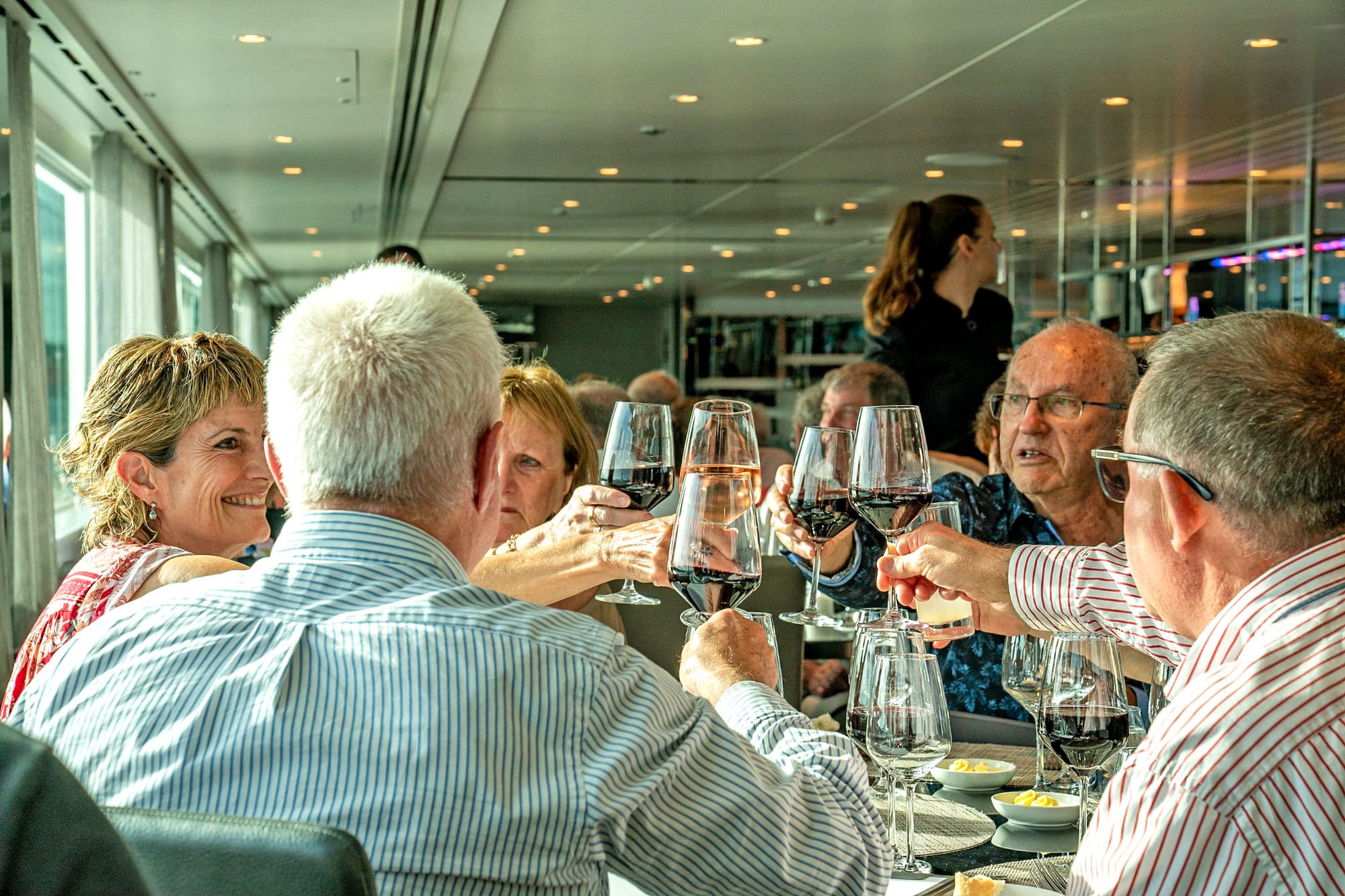 Several old white people cheers-ing glasses of wine on a river cruise ship