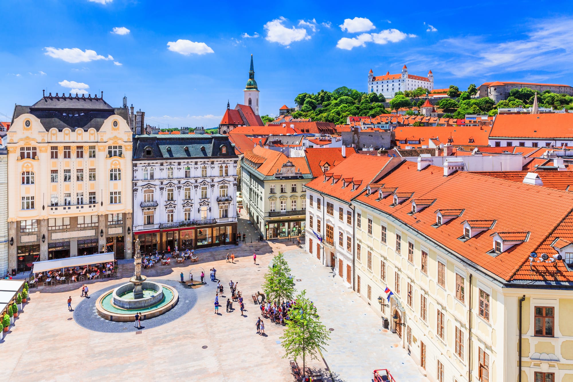An image of a town square with a hilltop fortress in the background during a sunny day